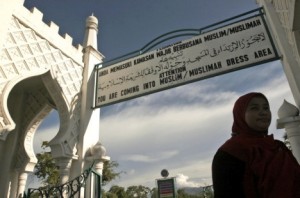 A woman walks past by a sign advising people to wear Muslim attire at Baiturrahman Grand Mosque in Banda Aceh. A local lawmaker says a controverisial bill allowing Shariah-style stoning and caning has gone into effect in the province. (Photo: Heri Juanda, AP)